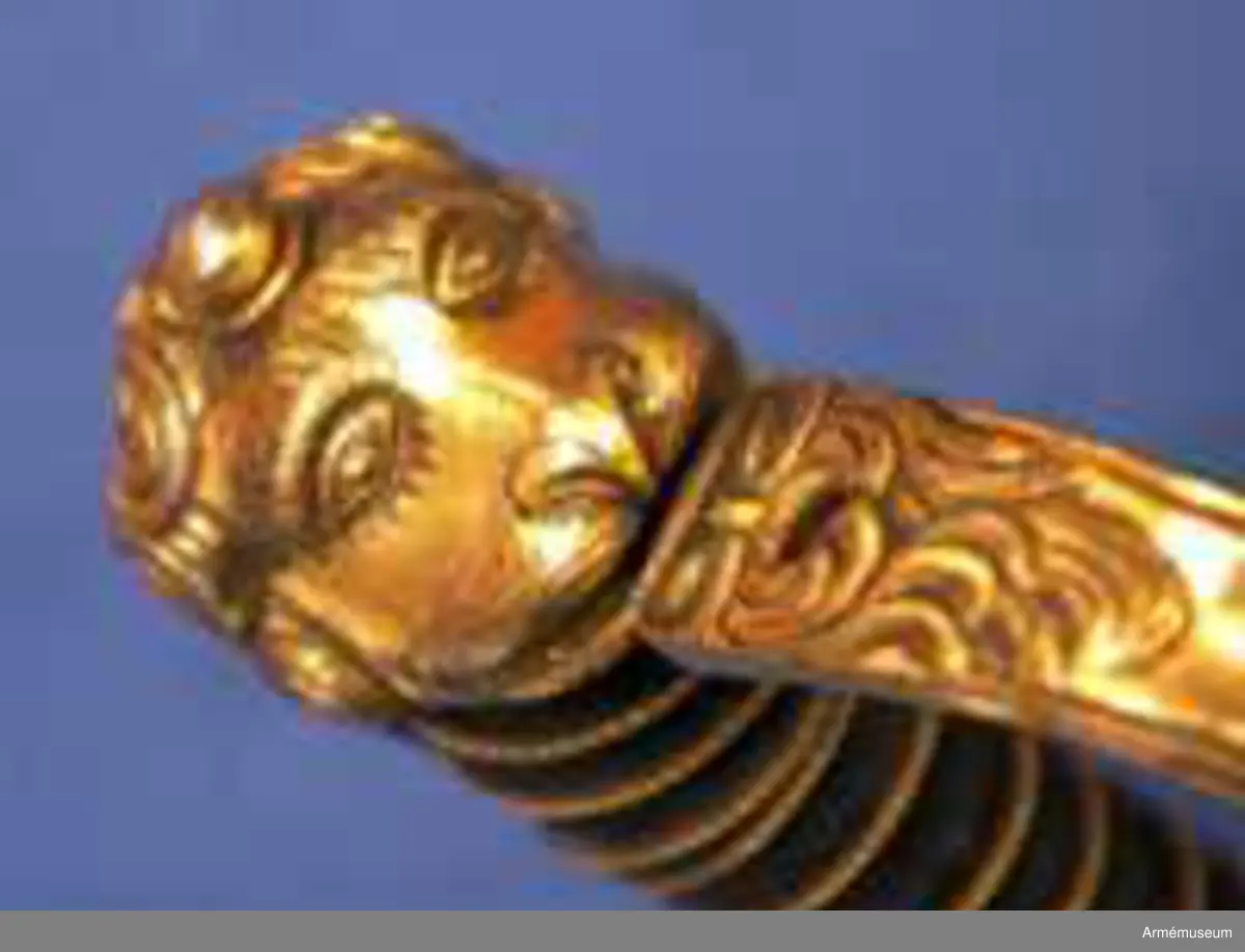 Klingans bredd upptill: 30 mm.Klingan är krökt, skålslipad och har nedtill en svart  betonad, tveegad klack. Fästet är av förgylld mässing. Kaveln är klädd med svart skinn en spiralräffla 16 varv. I bottnen på denna räffla är en av två parter hopsnodd, tunn mässingtråd anbringad. Baktill har kaveln ryggbeslag, som upptill övergår i en kappa, vilken är ciselerad i form av ett lejonhuvud och på vilken sitter en liten nitknapp. Parerstången är en rak och har fyrkantigt tvärsnitt samt av- slutas baktill av en nedböjd, på sidorna med ett spiralornament prydd knapp. Från parerstången främre ände utgår handbygeln i rät vinkel. Handbygeln är längs mitten litet försänkt och har längs var och en av framsidans kanter en ingraverad rand. Litet framför kappan genombrytes den av ett runt hål, och kring detta hål finns ciselerade ornament vilka bilda en stiliserad krans. På yttersidan finnes en uppåtböjd, delvis genombruten parerplåt, som är prydd med krönt sköld med tre kronor, vilken sköld omgives av ett par palmkvistar, allt i ciselerat arbete. Från parerplåtens spets utgår en delvis genombruten och sparsamt med ciselerade ornament prydd S-formig spång, som går till hand- bygelns övre del. På innersidan finns en liknande men mindre, ej genombruten och ej ciselerad parerplåt, från vars spets en S-formig spång går till handbygeln, vilken den träffar något längre ned än ytter- spången. Innerspången prydes längs kanterna av ingraverad rand.