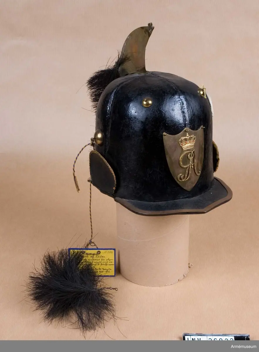 Kask med vapenplåt för manskap vid Västgöta (linje-)dragonregemente, troligen 1805-1807. Inrättad för plym som fattas. Vapenplåt med Gustaf IV Adolfs namnchiffer.