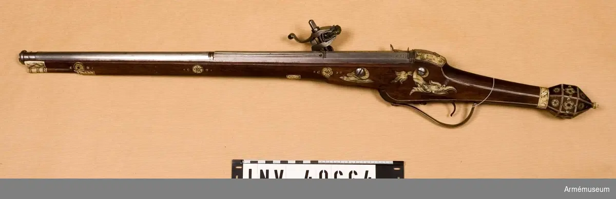 Grupp E III.
Pistolen är fullkomligt lik AM 40663, utom i att längs varbygelns undersida går en ingraverad rand. Dessutom har laddstaken, som även här är av trä med skoning av gravarat ben, i smaländan ett 9.5 cm långt järnbeslagen, i vilket finnes ett gängat hål för en krats. Den framtill på framstockens högra sida befintliga graverade benskivan med hål för främre pipsitift är utfallen.