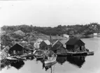 Skrivet på baksidan: Norge Vestagder Flekkevåg
Strandparti med bodar. Obs i bakgrunden, vadräckor. Den störr båten är en räktrålare.