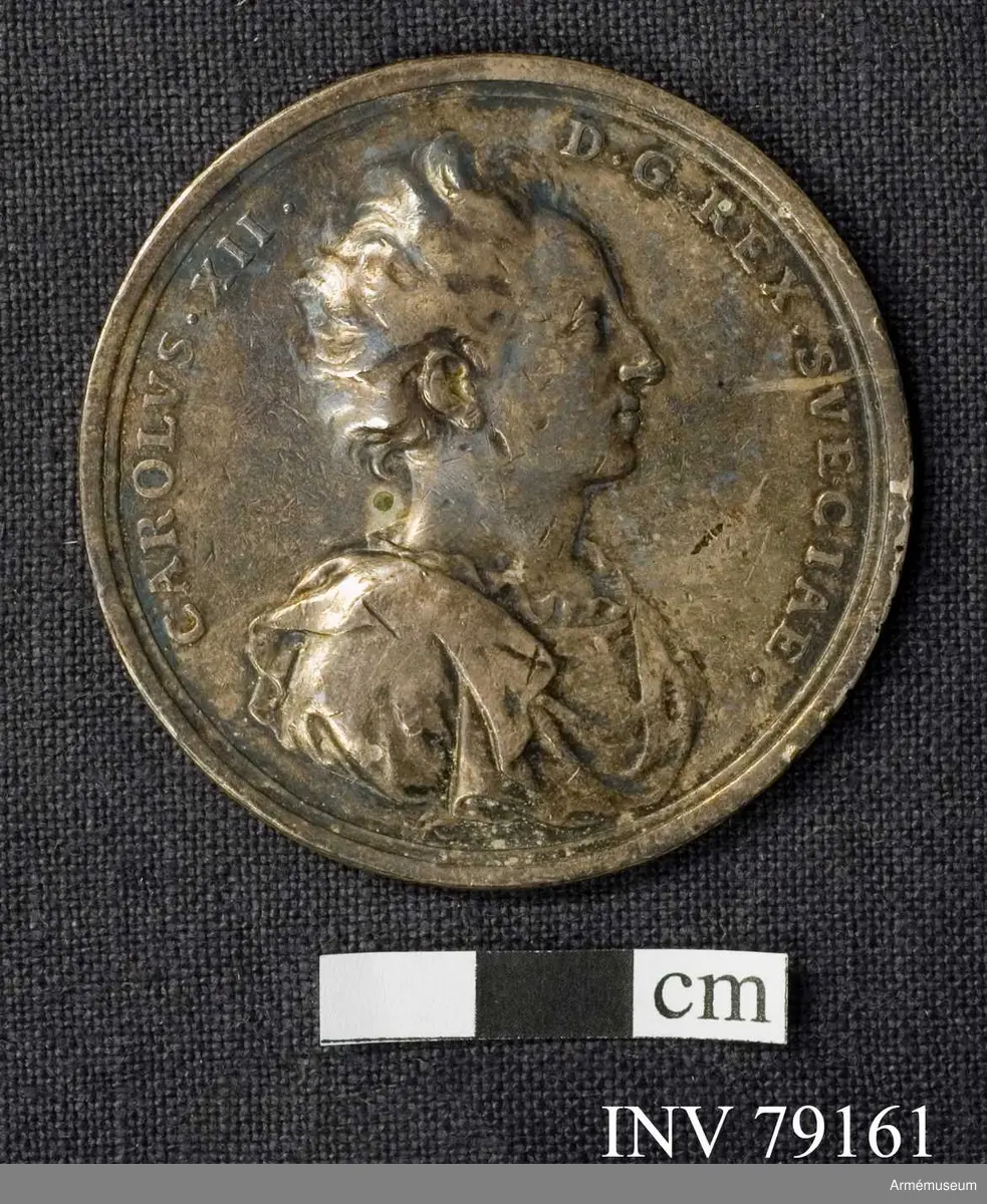 Grupp: M. 
Åtsidan: CAROLVS XII D G REX SVECIAE. Bröstbild åt höger, i slätt harnesk och släta mantelveck vikta över axeln, halsen bar med en veckad remsa över kanten av harnesket - Nedanför AC. 

Frånsidan: OB. PERDOMITVM CONTVMAX THORVNIVM. Segergudinnan, med palmqvist i venstra handen, sätter en lagerkrans på konungen, som står med åskvigg i sin hand - I avskärningen: MDCC III. 

Medaljen präglad av A. Karlsten.