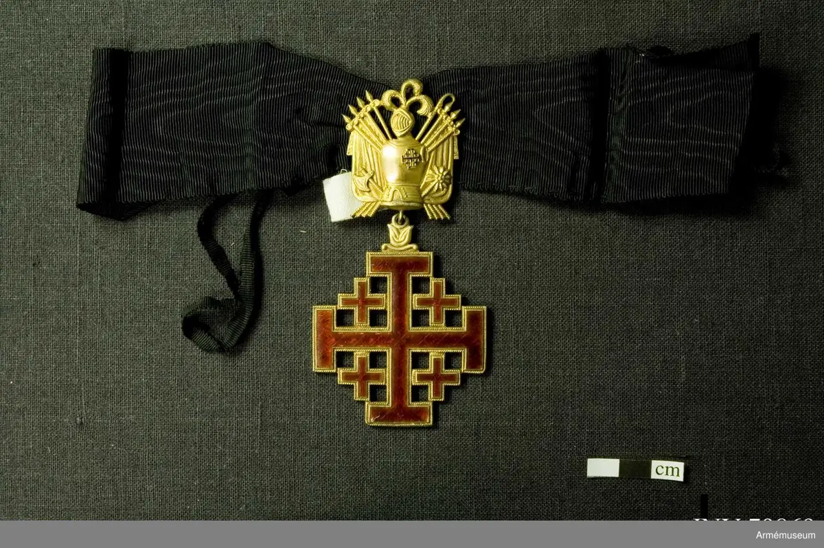 Påvliga Heliga Gravens orden, kommendörstecken i svart band. 
Miniatyr och knapp. Ordenstecknet i form av pilgrimssnäcka tilldelades ordensriddare som genomfört en pilgrimsresa till det heliga landet.

Förvaras i samhörande etui.