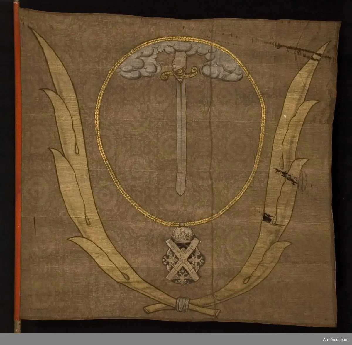 Duk av brun kinesisk sidendamast. Dekor i intarsia och målade detaljer. Motivet föreställer en hand med svärd som kommer ner ur ett moln omgivet av andreasordens kedja med dess insignier nedtill. Det hela omgivet av nedtill korslagda palmkvistar.
Slät, grönmålad stång. Spetsen bevarad.