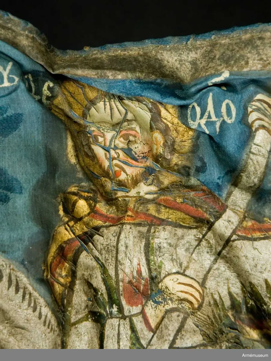 Entungad lansfana. Duk av blå kinesisk sidendamast med målad dekor. I 1703 års inventarium anges motivet vara St Göran men enligt den ryska inskriptionen är det Feodor Stratilat . Rosor och stjärnor av silver. Duken kantad med en silverbård. Strumpa av rött linne.