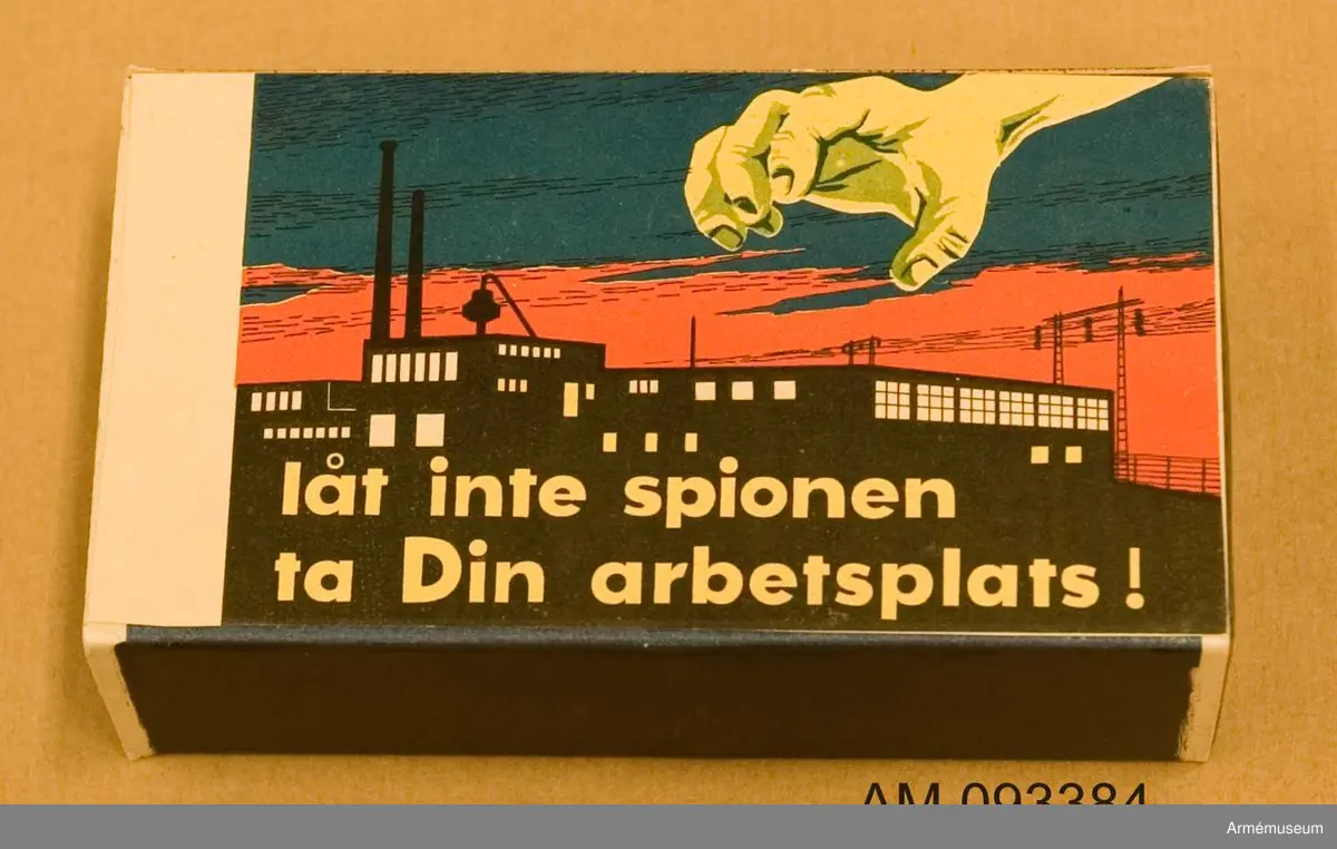 Tändsticksask med tändstickor. På ena sidan motivet Tre stjärnor och på andra sidan ett motiv som illustrerar hur en spionhand sträcker sig över en industribyggnad nattetid.