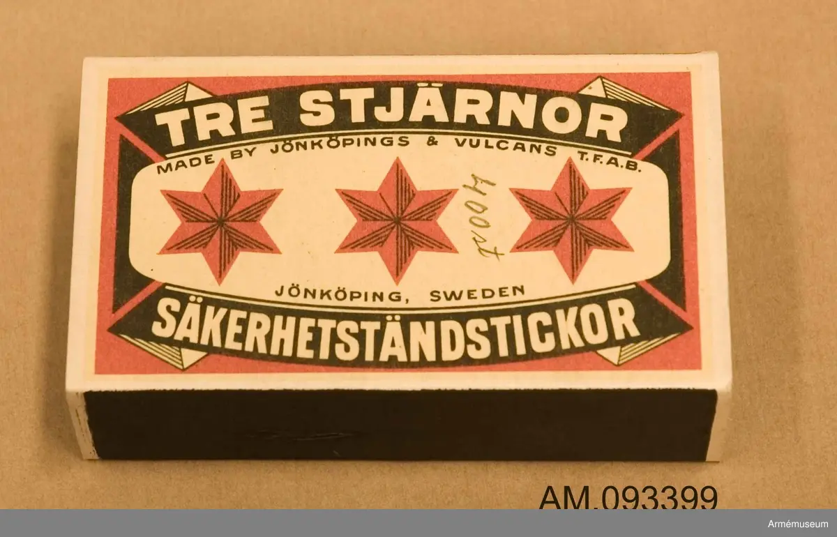 Tändsticksask med tändstickor. På ena sidan motivet Tre stjärnor och på andra sidan ett klistermärke med motivet en spionhand sträcker sig över en industribyggnad nattetid.