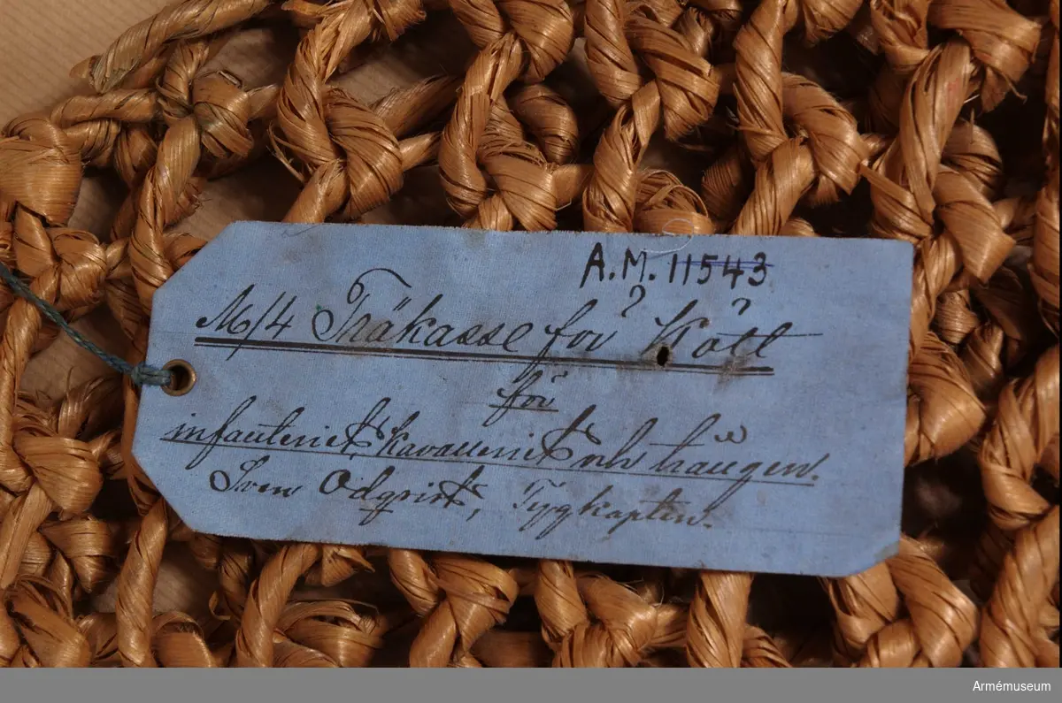 Kasse tillverkad av träbast bunden i runda maskor. Vidhängande blå pappersetikett med text: "No 4 Träkasse för kött, för infanteriet, kavalleriet och trängen. Sven Odquist, tygkapten"  KTS 2012-02-01