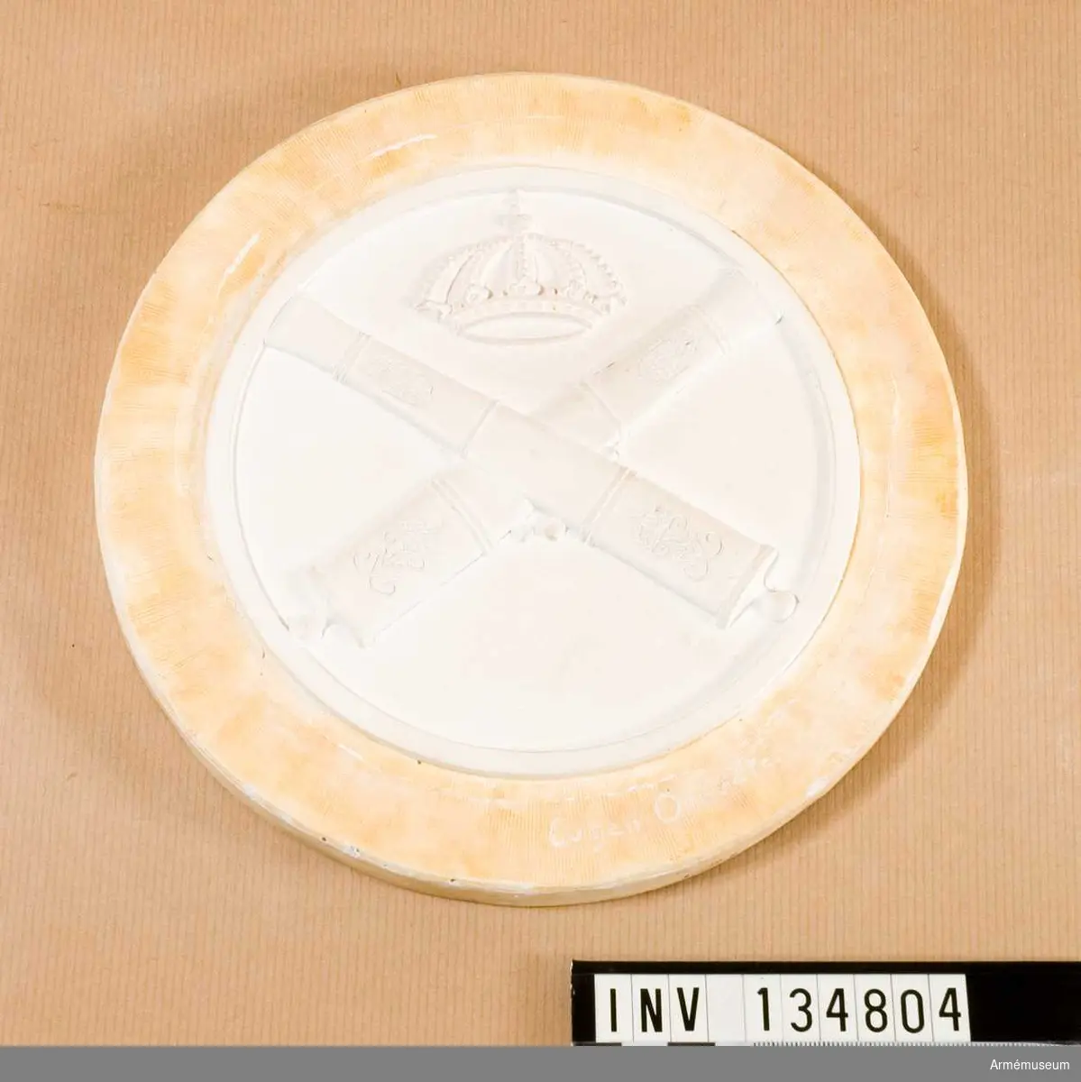 Gipsmodell med emblem för Artilleridepmentet, vagnmärke.
Nr. 63 enligt förteckning från Sporrong.