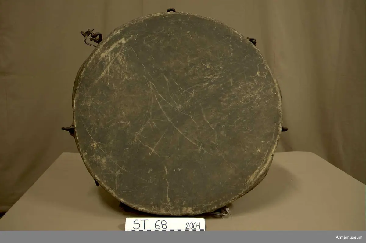 Kittel av koppar och skinn av kalv med fast spännring. Tredelad fot av järn. 7 skruvar och skruvfästen av järn. Bärrem av kalvskinn i två lager med spänne av järn.