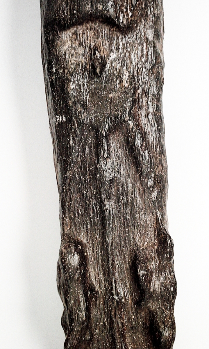 Skulpterad pilaster föreställande en herm eller möjligtvis en karyatid, under jonisk kapitäl.
Huvudet är vridet åt vänster samt prytt med en krona. Armarna hålls sträckta utefter sidorna.
Kroppen övergår i det med blad- och blomornamentik rikt sirade pilasterskaftet som smalnar av nedåt. Skaftet avgränsas genom en enkel vulst eller list från den rikt sirade och mjukt utbuktande piedestalen. Nedtill är piedestalen försedd med en bred bas. Skulpturens baksidan är slät.
Skulpturen är sliten.

Text in English: Sculptered pilaster with a Herm, or possibly a Caryatid, beneath an Ionic capital.
The head, with a crown, is turned to the left. The arms are streched out along the sides.
The body extends into the shaft of the pilaster, which tapers downwards and is richly decorated with leaf and flower ornamentation. A simple torus or batten separates the shaft from the richly decorated, softly bulging pedestal that has a broad base. The back of the sculpture is smooth.
The sculpture is worn.