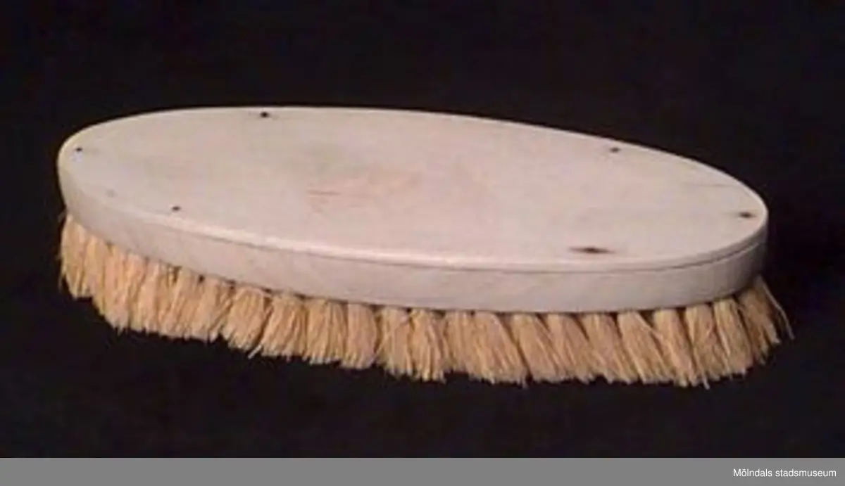 Oval badborste. Ovansida av bok. Borsten av ljust gul, sträv växtfiber.Blekta, urtvättade, lite spruckna.