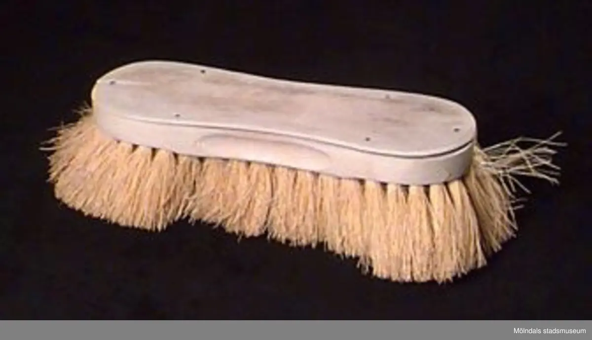 Avlång badborste som är insvängd på mitten och rundad i ändarna. Ovansida av bok. Borsten av ljust gul, sträv tätt ihopsatt växtfiber.Blekt, urtvättad, lite sprucken.