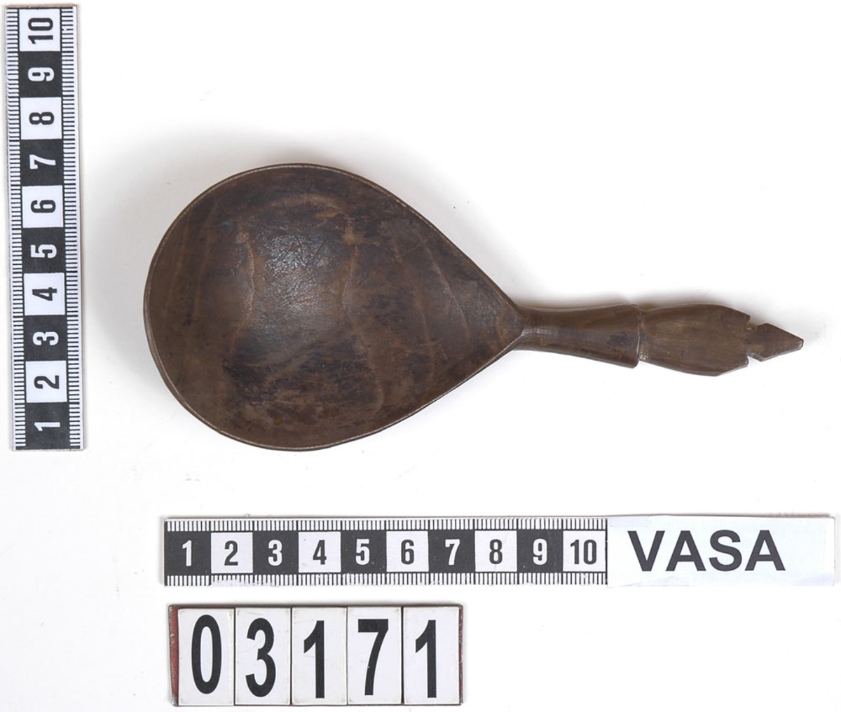 En träsked.
Skeden har ett ovalt skedblad och ett kort skaft. Skaftet är profilerat i tre avsatser. Skaftets ände är formad till en spets. På skeden syns spår av färg.
Skeden är mycket välbevarad, bortsett från en liten spricka som är synlig på baksidan.

Text in English: Wooden spoon with egg-shaped bowl and short, profiled handle ending in a point.
Intact and well preserved except for a small crack on the reverse.