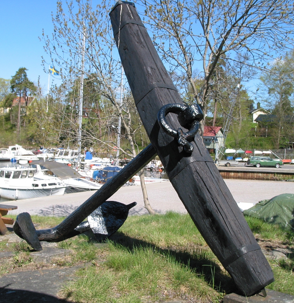 Stockankare. Trästock med fyra järnband samt en skyddskåpa i metall över ändträet på övre delen. Stockens två delar hålls ihop med fyra kilade trädymlingar. Stocken är på vissa partier mycket sliten. Schackel i röringen.