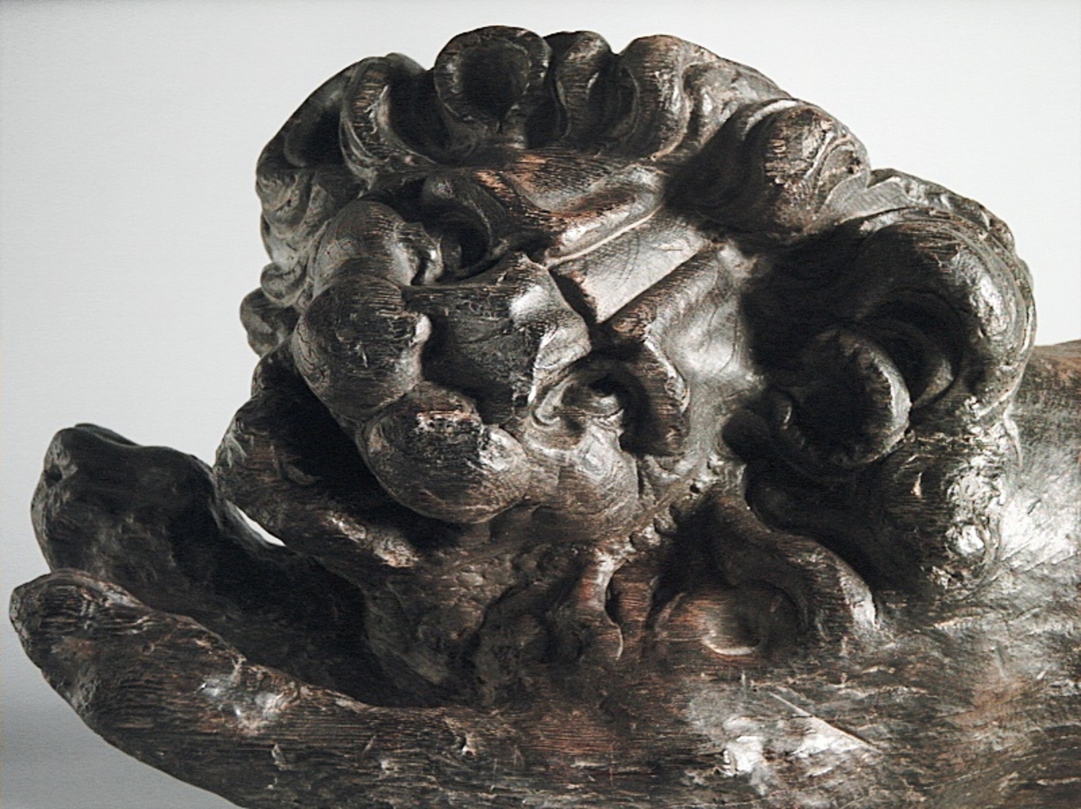 Skulptur av ett litet, liggande lejon med utsträckta framben och hopdragna bakben.
Lejonet är riktat mot vänster, sett från betraktaren. Det snett hållna huvudet återges i det närmaste i en face. Större delen av svansen saknas. Den befintliga delen av svansen avtecknar sig mot lejonets vänstra lår.

Lejonet är endast delvist rundskulpterat. På baksidan, i höjd med huvudet och höger framben, återfinns ett stort, snett urtag som bildar en slät anliggningsyta. Skulpturens framparti är således endast till hälften så tjockt som dess bakparti.
Bakkroppen är kraftigt sliten och skadad. Vänster bakben saknas, liksom större delen av svansen.

Text in English: Sculpture of a small reclining lion with its forelegs extended and its  hind legs tucked beneath its body.
Facing to the observer''s left, the head, held crookedly, is nearly en face. A large part of the tail is missing, and the remainder curves towards the left hind leg.

The lion is only partly three-dimensional. On the rear at the head height and at the right foreleg a large oblique hole forms a flat area for attachement, thus the forepart of the sculpture is thus only half as thick as its rear.
The rear of the body is badly worn and damaged. The left hind leg has been broken off.