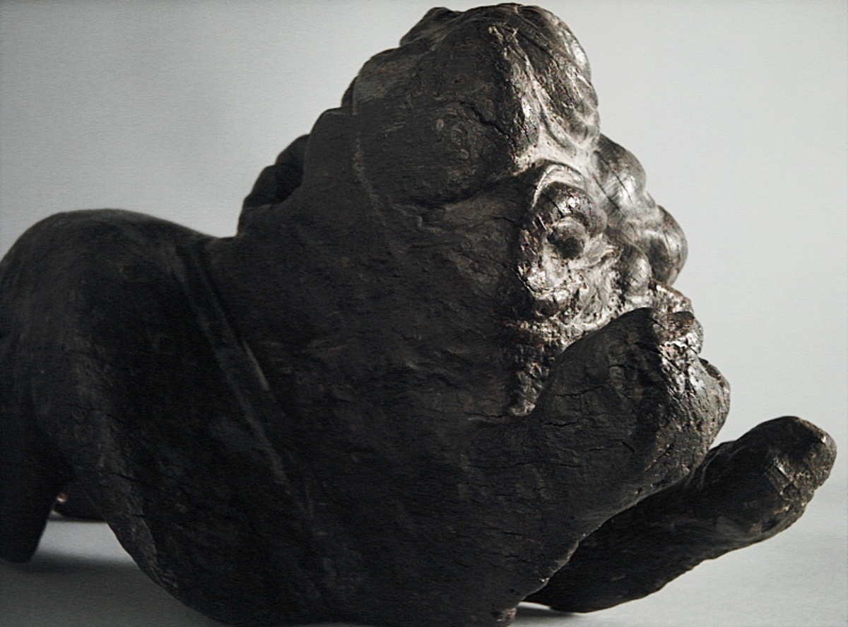 Skulptur av ett litet, liggande lejon med utsträckta framben och hopdragna bakben.
Lejonet är riktat mot vänster, sett från betraktaren. Det snett hållna huvudet återges i det närmaste i en face. Större delen av svansen saknas. Den befintliga delen av svansen avtecknar sig mot lejonets vänstra lår.

Lejonet är endast delvist rundskulpterat. På baksidan, i höjd med huvudet och höger framben, återfinns ett stort, snett urtag som bildar en slät anliggningsyta. Skulpturens framparti är således endast till hälften så tjockt som dess bakparti.
Bakkroppen är kraftigt sliten och skadad. Vänster bakben saknas, liksom större delen av svansen.

Text in English: Sculpture of a small reclining lion with its forelegs extended and its  hind legs tucked beneath its body.
Facing to the observer''s left, the head, held crookedly, is nearly en face. A large part of the tail is missing, and the remainder curves towards the left hind leg.

The lion is only partly three-dimensional. On the rear at the head height and at the right foreleg a large oblique hole forms a flat area for attachement, thus the forepart of the sculpture is thus only half as thick as its rear.
The rear of the body is badly worn and damaged. The left hind leg has been broken off.