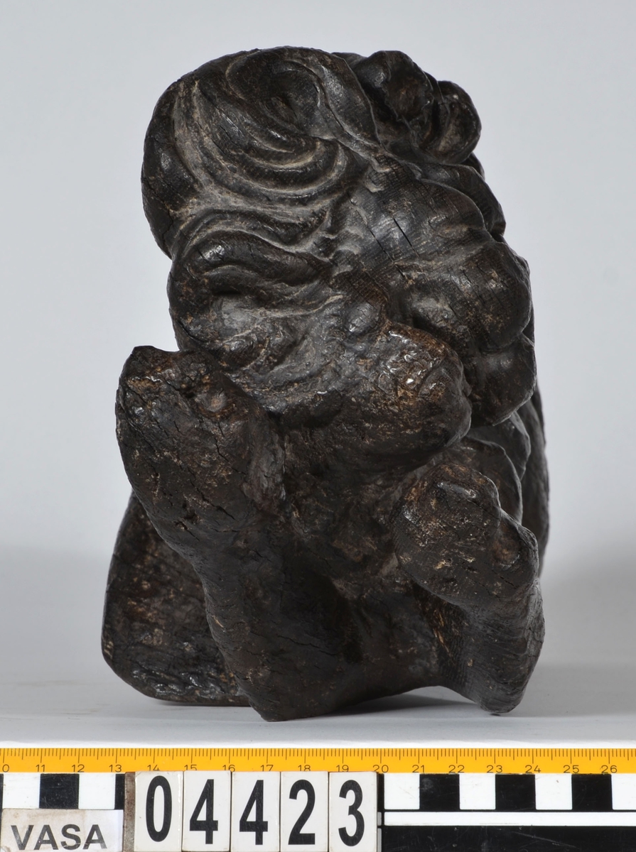 Skulptur av ett litet, liggande lejon med utsträckta framben och hopdragna bakben.
Lejonet är riktat mot vänster, sett från betraktaren. Det snett hållna huvudet återges i det närmaste i en face. Större delen av svansen saknas. Den befintliga delen av svansen avtecknar sig mot lejonets vänstra lår.

Lejonet är endast delvist rundskulpterat. På baksidan, i höjd med huvudet och höger framben, återfinns ett stort, snett urtag som bildar en slät anliggningsyta. Skulpturens framparti är således endast till hälften så tjockt som dess bakparti.
Bakkroppen är kraftigt sliten och skadad. Vänster bakben saknas, liksom större delen av svansen.

Text in English: Sculpture of a small reclining lion with its forelegs extended and its  hind legs tucked beneath its body.
Facing to the observer''s left, the head, held crookedly, is nearly en face. A large part of the tail is missing, and the remainder curves towards the left hind leg.

The lion is only partly three-dimensional. On the rear at the head height and at the right foreleg a large oblique hole forms a flat area for attachement, thus the forepart of the sculpture is thus only half as thick as its rear.
The rear of the body is badly worn and damaged. The left hind leg has been broken off.