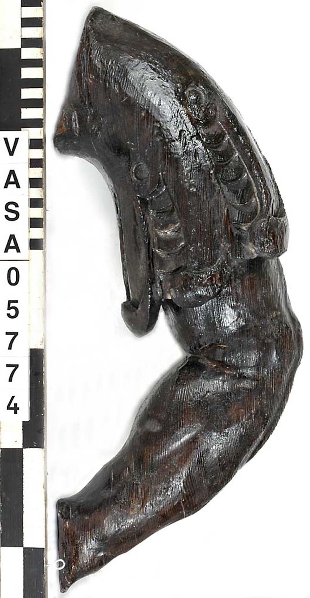Del av skulptur. Arm till Stora krigaren på babord sida. Mycket kraftig. Bruten. Saknar hand samt en del av klädnadens ärm. Vackert snidad. Konstnären har använt sig av träets ådring för att få fram musklernas form.

Text in English: Arm belonging to sculpture. Very worn, broken.