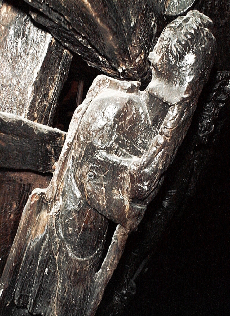 Skulptur föreställande en mansfigur med långt hår och ett stort böljande patriarkskägg. Pannan är rynkad. På huvudet sitter en stor, slät hjälm med långa, nedhängande plymer. Figuren är iförd en enkel dräkt, en rustning av thoraxmodell eller möjligen en civil dräkt. Vid vänster sida hänger från bältet en oval sköld med bred kant. Figuren stödjer sig mot en stav.



Figurens huvud är kraftigt vridet åt vänster medan bålen, främst dess övre del, är vriden något åt höger. Benen är frontalställda och korslagda. Kroppstyngden vilar helt på det vänstra benet. Det högra benet är placerat framför det vänstra. Figuren stödjer armarna mot en stav, med överkroppen något framåtlutad. Figuren står på en sockel, vilken pryds av en namninskription.



Skulpturens baksida uppvisar tre snedställda, olika djupt liggande fält. Fälten, som utgör anliggningsytor, ger skulpturen en trappstegsformad profil.

Skulpturen är relativt sliten. Figurens händer är till största delen bortnötta. Höger underben med fot saknas. Staven är avbruten nedtill. Ursprungligen har skulpturens bakstycke varit framdraget i en "huvudplatta", som dock är bortbruten, liksom det översta fältet på skulpturens baksida. Namninskriptionen är ej läsbar.



Text in English: A sculpture representing a male figure with a wrinkled forehead, long hair and a long, fluttering beard. On the head is a smooth helmet with long, hanging plumes. The figure is wearing armour - probably of thorax type - or some sort of civilian dress. An oval shield with a broad edging hangs from the belt.



The figure appears to be leaning forward on a staff with the body weight on itÂ´s left leg and the right leg crossed over in front of the left leg. The legs and the lower part of the body face forward and are upright, while the upper part of the torso leans forward towards the right. The head is turned to look over the left shoulder. The figure stands on a plinth with an inscription.



The sculpture''s back has three obliquely placed surfaces of different depths that are areas of attachment. The surfaces make the sculpture look like a step-ladder in profile.

The sculpture is rather worn, the hands are almost completely worn away, the lower part of the right leg is missing, and the lower part of the staff is broken. The upper part of the back board is broken off. The  inscription is illegible.