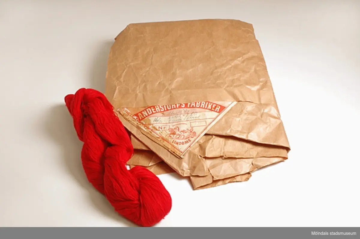 Rött bomullsgarn 16/2 i härva, avsett för vävning av bomullstyg. Garnet låg förpackat i brunt omslagspapper med etikett från Anderstorps fabriker, Lindome. Givaren fick garnet av sin svärmor. Det hade blivit över, när hon vävt tyg till sin hembygdsdräkt. Garnet var specialbeställt och specialfärgat för tillverkning av denna dräkt. Färgningen skedde vid Anderstorps fabrik i Lindome. Fabriken ägdes av August Werner.