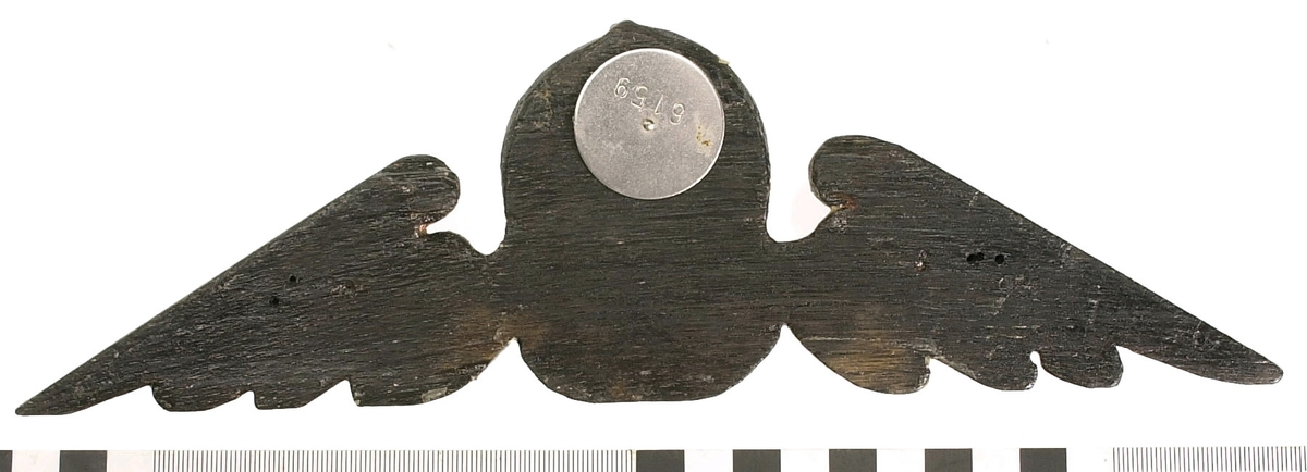 Kerub.
Skulptur i form av ett litet, runt kerub- eller gummansikte med böjd näsa, liten mun, tjocka kinder och kraftigt rynkad panna.
Ansiktet inramas helt av en tättslutande, mössliknande huvudbonad med flikig framkant. Den kombineras med en bred krage från vilken det utgår dekorativt formade vingar med pålagda broskornament. Baksidan är slät.
Skulpturen är mycket välbevarad.

Text in English: Sculpture of a small, round face of an old woman or cherub, with a curved nose, small mouth, plump cheeks, and heavily wrinkled forehead.
The face is wholly framed by a close-fitting covering like a night cap with a lobed front edge. This is combined with a wide collar from which extend large decoratively formed wings with applied earshell work. The back is flat.
The sculpture is very well preserved.