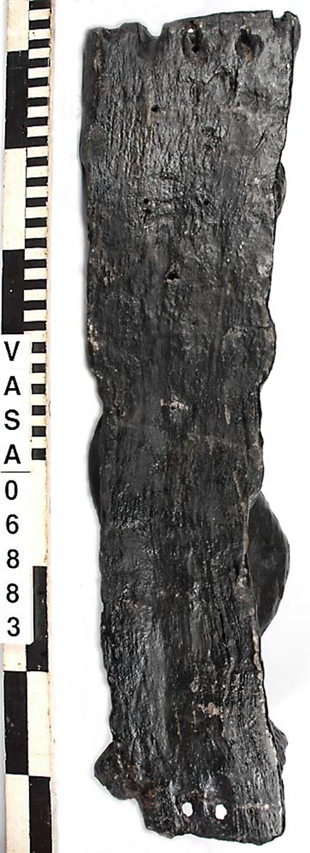 Skulptur föreställande en barnfigur spelande en harpa.
Instrumentet hålls med bägge händerna. Huvudet är vridet något åt höger. Kroppstyngden vilar på vänster ben medan höger ben är böjt. Vid höger sida syns en mantel. Ovanför hjässan sitter en snedställd äggstavslist. Figuren står på ett minimalt underlag som troligen avser att föreställa ett stycke naturlig mark. Skulpturens baksida är slät.
Skulpturen är mycket sliten.

Text in English: This is a sculpture of a child playing a harp.
The instrument is held in both hands. The head is turned slightly to the right. The weight of the body rests on the left leg, the right leg is bent. A mantle is to be seen to the figures right side. Just above the head the back board comes foreward at right angles and the front of the board is wide and is decorated with an egg moulding design which is placed diagonally across it with the right-hand side lower than the left-hand side, when the sculpture is viewed from the front. The figure stands upon a small flat plinth. The back of the sculpture is smooth.
The sculpture is very  worn.