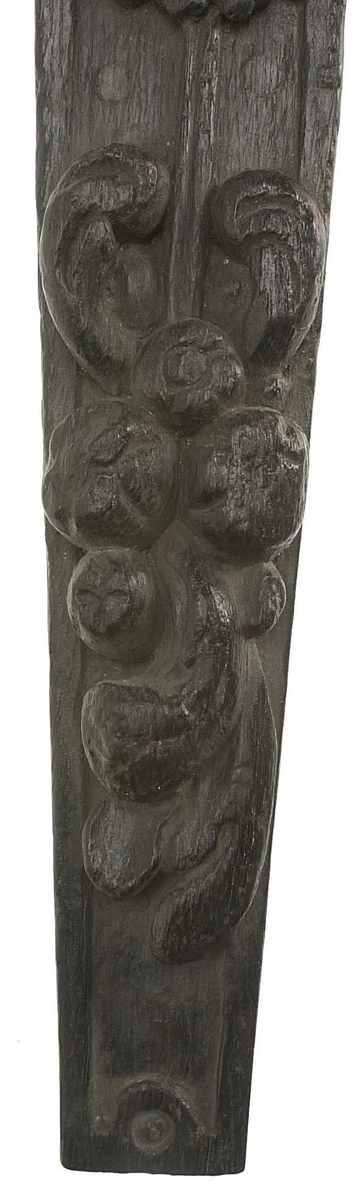 Hermpilaster.
Liten skulpterad pilaster föreställande skäggig herm under joniskt kapitäl.
Huvudet är vridet mot vänster. Hermen är insvept i en mantel som hålls fast med vänster hand framför magen. I höger hand håller figuren ett okänt föremål (blomsterkälk?) framför bröstet. Pilasterskaftet är prytt med stora frukter och blad, fasthängande vid en stängel som delvis täcker det nedåt avsmalnande skaftets ramverk. Baksidan är slät.
Skulpturen är mycket välbevarad med sju spikhål.

Text in English: Small sculpted pilaster with a bearded Herm beneath an Ionic capital.
The head of the figure is turned to the left. The Herm is enveloped in a mantle, held fast with the left hand in front of its stomach. Its right hand holds an unknown object (a bunch of flowers?) in front of its breast. The shaft of the pilaster is decked with large fruit and leaves hanging from a stalk which partly cover the framing of the tapering shaft. Its back is flat.
The sculpture is very well preserved.