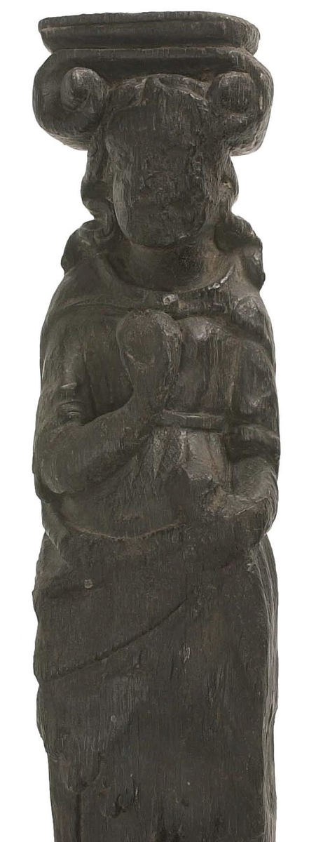 Hermpilaster.

Liten pilaster i form av en karyatid, med långt böljande hår under joniskt kapitäl.

Huvudet är vridet en aning åt höger. Med vänster hand hålls manteln samlad. I höger hand håller figuren en frukt eller dylikt framför bröstet. Pilasterskaftet är prytt med stora frukter och blad, fasthängande vid en stängel som delvis täcker det nedåt avsmalnande skaftets ramverk. Baksidan är slät.

Skulpturen är välbevarad, förutom ansiktet som är kraftigt slitet.

Fyra stycken spikhål, en övertäckt med en plugg.


Text in English: Sculpted small pilaster with a Caryatid with long wavy hair beneath an Ionic capital.

Its head is turned slightly to the right, its left hand holds its gathered mantle. Its right hand holds fruit or the like in front of its brests. The shaft of the pilaster is decorated with fruit and large leaves hanging from a stalk, which partly cover the framing of the tapering shaft. Its back is flat.

The sculpture is somewhat worn, its facial expression has been obliterated.