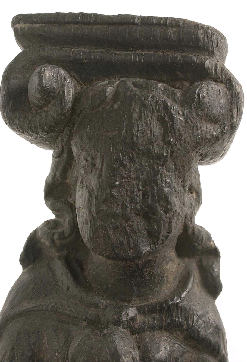 Hermpilaster.

Liten pilaster i form av en karyatid, med långt böljande hår under joniskt kapitäl.

Huvudet är vridet en aning åt höger. Med vänster hand hålls manteln samlad. I höger hand håller figuren en frukt eller dylikt framför bröstet. Pilasterskaftet är prytt med stora frukter och blad, fasthängande vid en stängel som delvis täcker det nedåt avsmalnande skaftets ramverk. Baksidan är slät.

Skulpturen är välbevarad, förutom ansiktet som är kraftigt slitet.

Fyra stycken spikhål, en övertäckt med en plugg.


Text in English: Sculpted small pilaster with a Caryatid with long wavy hair beneath an Ionic capital.

Its head is turned slightly to the right, its left hand holds its gathered mantle. Its right hand holds fruit or the like in front of its brests. The shaft of the pilaster is decorated with fruit and large leaves hanging from a stalk, which partly cover the framing of the tapering shaft. Its back is flat.

The sculpture is somewhat worn, its facial expression has been obliterated.