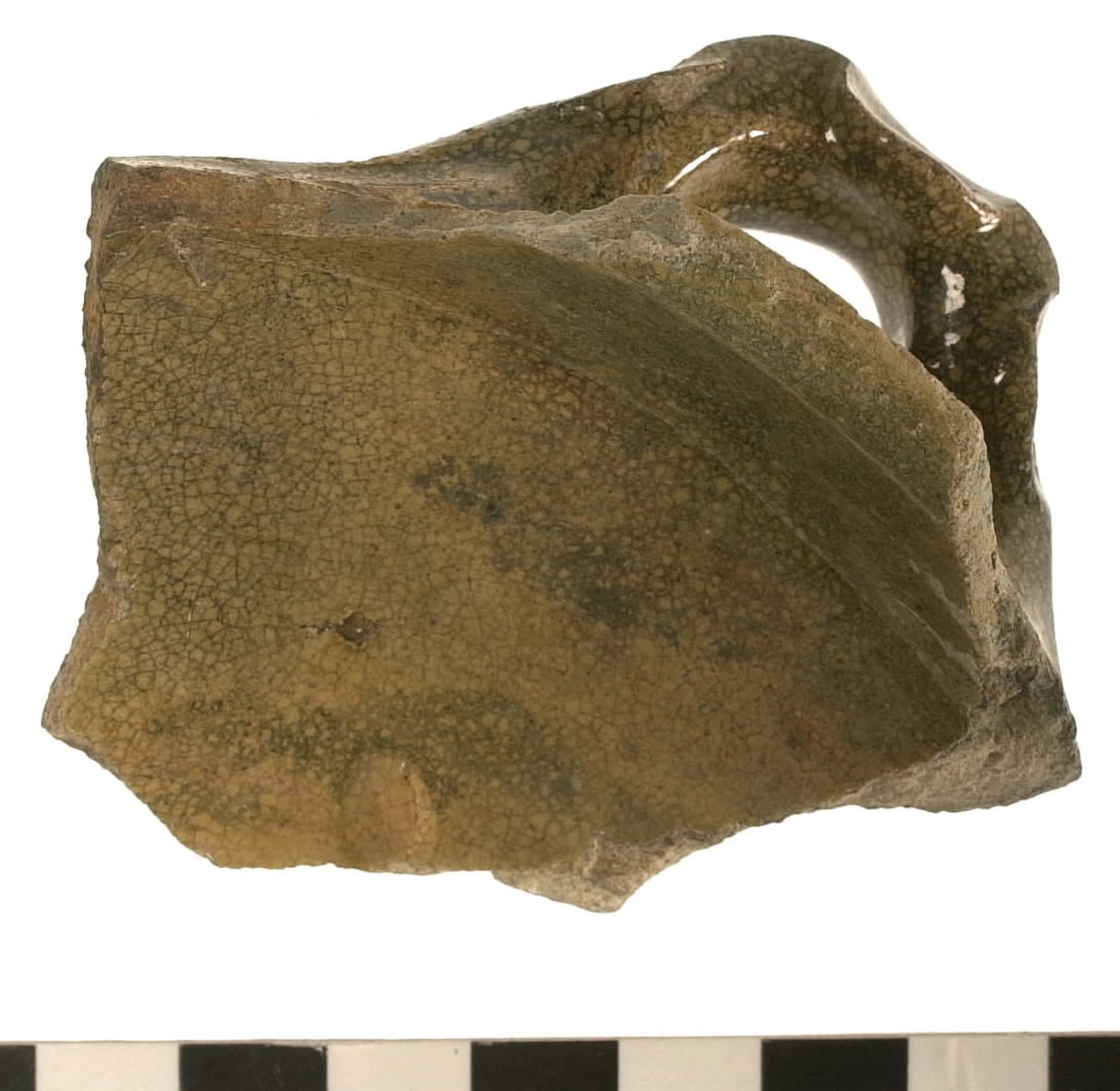 Del av skål.
1 st vertikal bandhänkel, tummad, 70 x 60 mm. Fragment av mynningsrand och buk. In- och utsida blyglaserad gulgrön.