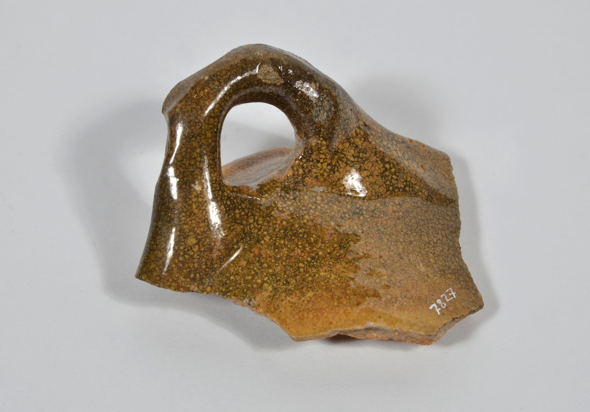 Del av skål.
1 st vertikal bandhänkel, tummad, 70 x 60 mm. Fragment av mynningsrand och buk. In- och utsida blyglaserad gulgrön.