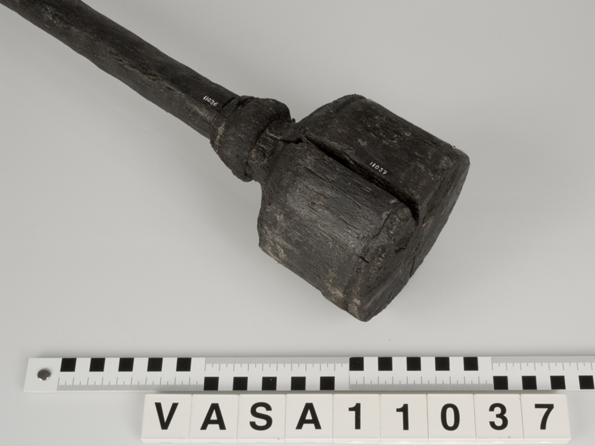 Kolv till ansättare. Kolven består av ett cylindriskt, svarvat, trästycke med ett centrerat skafthål. I övre änden, åt skaftet till, är kolven profilsvarvad. Motsatt ände är platt. Några sprickor, annars i fint skick.