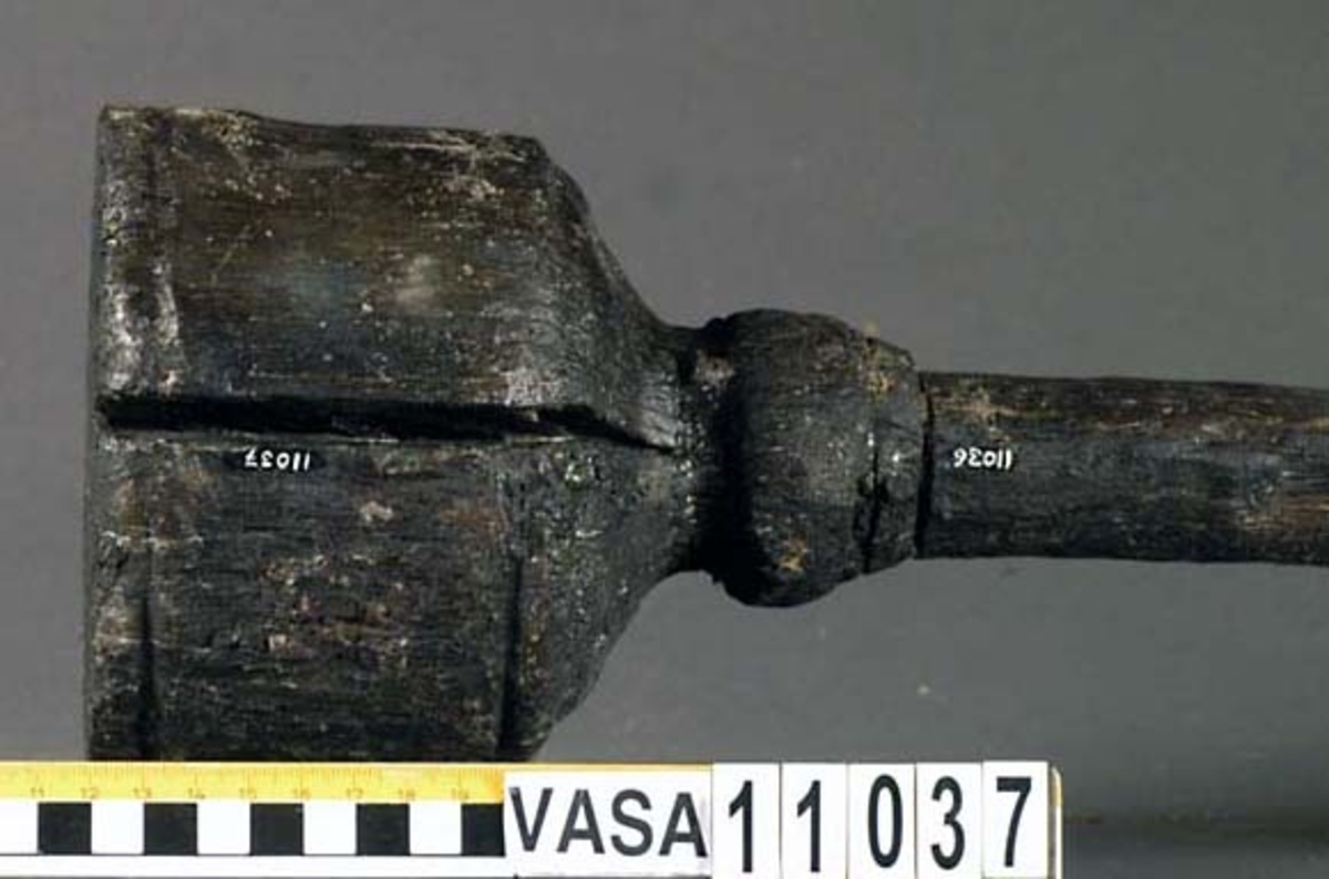 Kolv till ansättare. Kolven består av ett cylindriskt, svarvat, trästycke med ett centrerat skafthål. I övre änden, åt skaftet till, är kolven profilsvarvad. Motsatt ände är platt. Några sprickor, annars i fint skick.