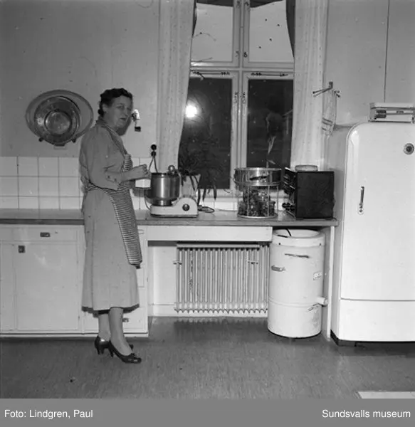Fru Lindlöf i sitt kök, samt två pojkar som hjälper till med disken.