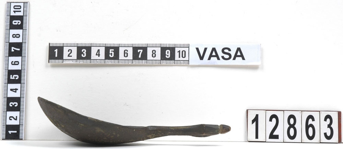 En träsked. Skeden har ett ovalt skedblad och ett kort skaft. Skaftets ände är rombformat samt försett med en liten knopp. På skedbladet syns en inristad dekor.

Skeden är välbevarad och har synliga färgspår.

För mer information se Dokumentationsblankett under Referenser – Länkade filer.