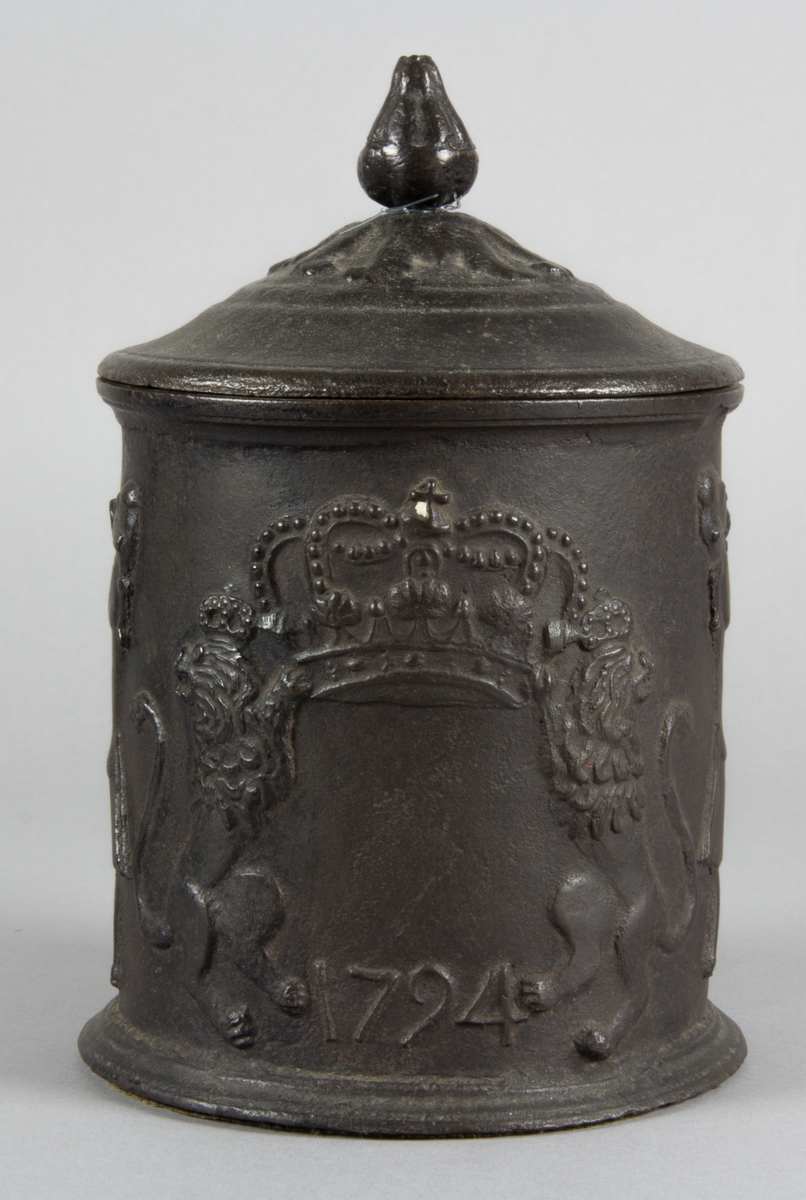 Relief på burken med text. Relief med rökande och spelande män. Några av männen sitter vid en spis. Riksvapen med flankerande lejon. Årtal 1794.
Text på burken. ORE FUMOSO BENE BIBENTUR.