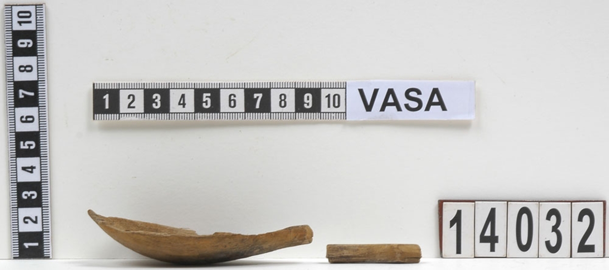 Fyra delar av en träsked. De två större delarna utgör skedskaftet samt större del av skedbladet med ett mindre parti av skaftet. De övriga två delarna utgör fragment av skedblad.

Insidan av skedbladet är dekorerad med ett ristat/glödritat vågmönster. Skedskaftet är kort och rakt, med profilerad skaftände. Längst ut på skaftänden syns en brottyta. Troligtvis har skaftet avlutats i en ändknopp. Skeden har gul-röda utfällningar samt rödbruna färgspår.

Skeddelarna är mycket ömtåliga, med sprickor.

För mer information se Dokumentationsblankett under Referenser – Länkade filer.