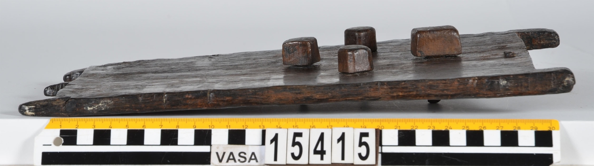 Rektangulärt träskrin med kombinationslås.



På lockets undersida sitter ett kombinationslås av trä. Låset består av en tretungad, gaffelliknande låsarm och tre låshjul. Låshjulen är försedda med var sitt inhak i vilka låsarmen låses fast. På lockets ovansida syns fyra, fyrkantiga pluggar till vilka låsarmen och låshjulen sitter fästade med trästift. Med hjälp av pluggarna regleras låshjulen och låsarmen. På vardera sida om låsarmen sitter ett mindre hål.



Lockets kortsidor är försedda med två respektive tre utstickande tappar. De två yttersta tapparna omsluter gaveln när locket är på. Den ena kortsidans mitttapp utgör låsregel. Skrinets gavlar är snedskurna upptill och har urtag på sidorna för inpassning av lockets tappar. Upptill på den ena gaveln finns ett fyrkantigt hål för låsarmen. Skrinets långsidor är falsade mot gavlarna och sitter fästade med tre trädymlingar vid varje gavelkant. På skrinets undersida finns ett hål med plugg samt tre bomärken.



Träskrinet är intakt och i gott skick, endast låsarmens trästift är rekonstruerade. Låsarmen har tidigare varit avbruten och det finns spår av lagningen i form av en tunn spricka. På skrinets ena gavel syns en spricka.



Text in English: A rectangular, undecorated box with a combination lock.



On one side of the lid is a wooden combination lock, consisting of four pegs on top that regulate a three-pronged bolt and three wheels underneath. Each wheel has a separate notch into which the bolt is inserted for locking. The bolt and wheels are each fitted to the square-shaped pegs with a small wooden pin. Situated on either side of the bolt is a small hole.



The sides are fixed by three dowels at the corners and the bevelled ends have notches on each side and a hole in the centre to fit the pegs of the lid. One end has a square-shaped notch for the bolt.



Underneath the box is a hole with a plug and three owner''s marks.

The box is intact except for the reconstructed pins. In good condition although there is a crack on one end of the box. The bolt was once broken but is now mended.