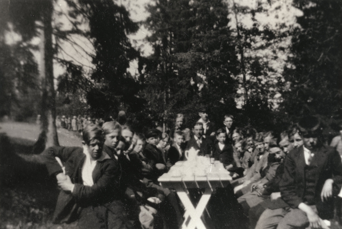 Pojkar sittande kring kaffebord i en park. Skolresa till Trollhättan. Åkte dit i likbil. Magister Villard Nilsson-Stockelids klass från Grevedämmets skola i Mölndal.