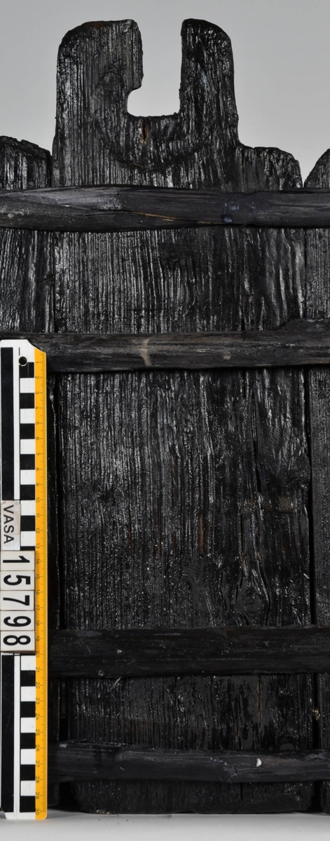 Laggstav till en balja. I stavens övre del finns ett urtag för en regel eller tvärslå. Urtaget är skadat och den övre delen saknas. Runt urtaget finns en fasad nedsänkning, eventuellt för någon form av beslag. På insidan av stavens nedre ände finns ett urtag. Urtaget är ett hugget spår där baljans bottenplatta sitter.