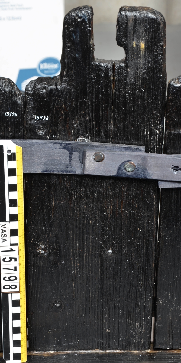 Laggstav till en balja. I stavens övre del finns ett urtag för en regel eller tvärslå. Urtaget är skadat och den övre delen saknas. Runt urtaget finns en fasad nedsänkning, eventuellt för någon form av beslag. På insidan av stavens nedre ände finns ett urtag. Urtaget är ett hugget spår där baljans bottenplatta sitter.