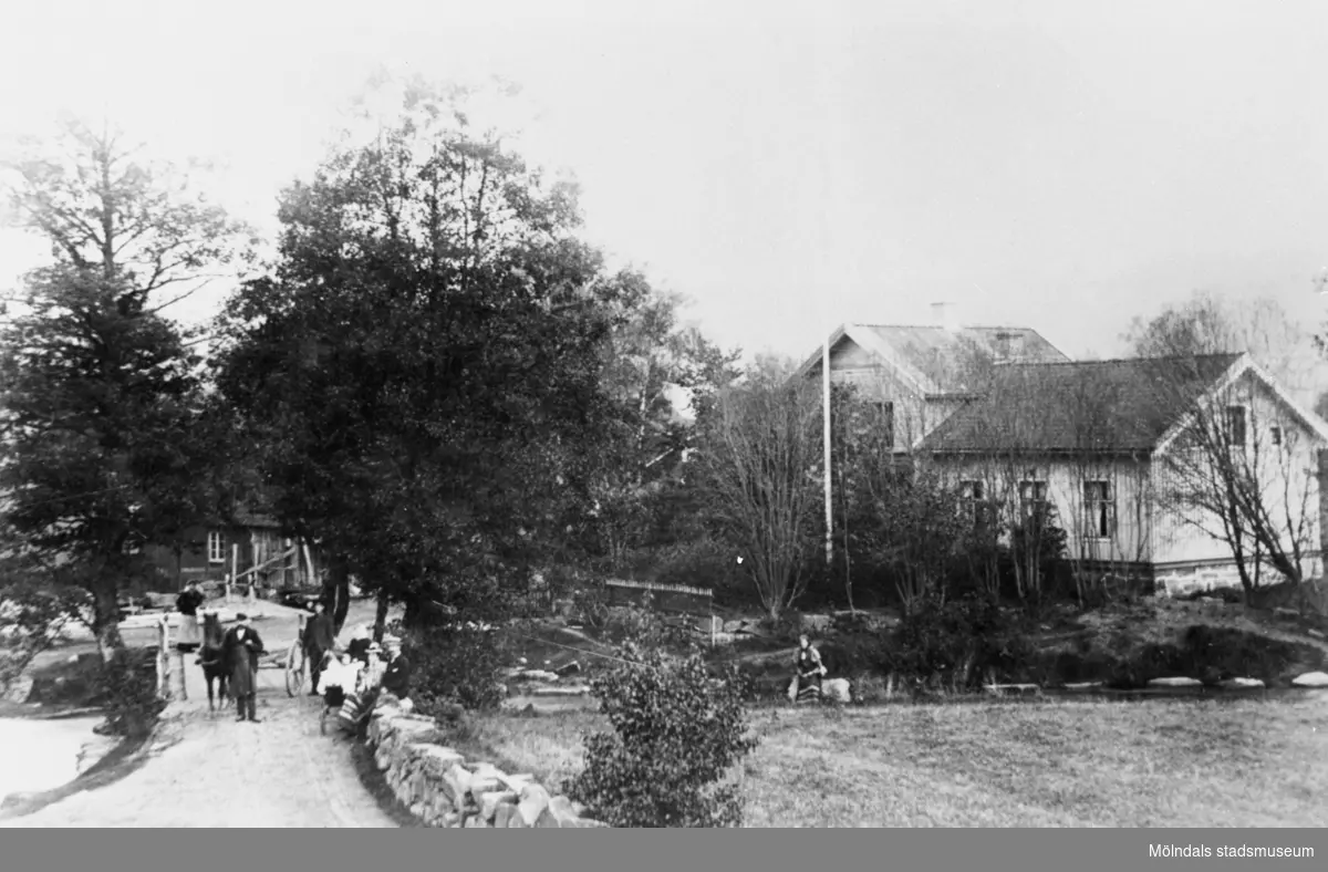 Hällesåkers bro i Lindome, 1907. Liten folksamling samt häst med kärra på bro.