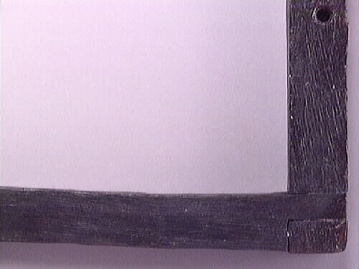 En vinkelhake.

Vinkelhaken består av två plana stavar som är sammanfogade genom sinkning. Ändarna är profilerade. I mitten av den kortare staven finns ett runt hål för upphängning.

Vinkelhaken är välbevarad och i gott skick.

För mer information se Dokumentationsblankett under Referenser – Länkade filer.