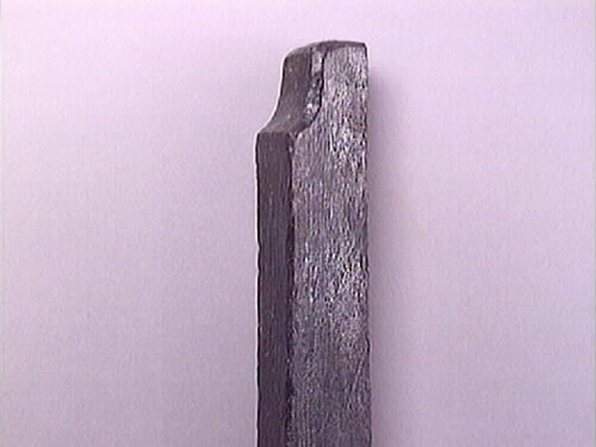 En vinkelhake.

Vinkelhaken består av två plana stavar som är sammanfogade genom sinkning. Ändarna är profilerade. I mitten av den kortare staven finns ett runt hål för upphängning.

Vinkelhaken är välbevarad och i gott skick.

För mer information se Dokumentationsblankett under Referenser – Länkade filer.