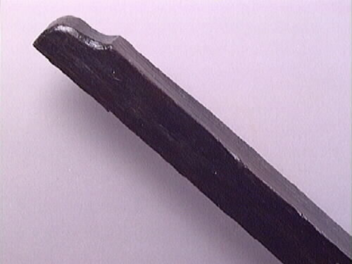 En vinkelhake.

Vinkelhaken består av två plana stavar som är sammanfogade genom sinkning. Ändarna är profilerade. I mitten av den kortare staven finns ett runt hål för upphängning.

Vinkelhaken är välbevarad och i gott skick.

För mer information se Dokumentationsblankett under Referenser – Länkade filer.