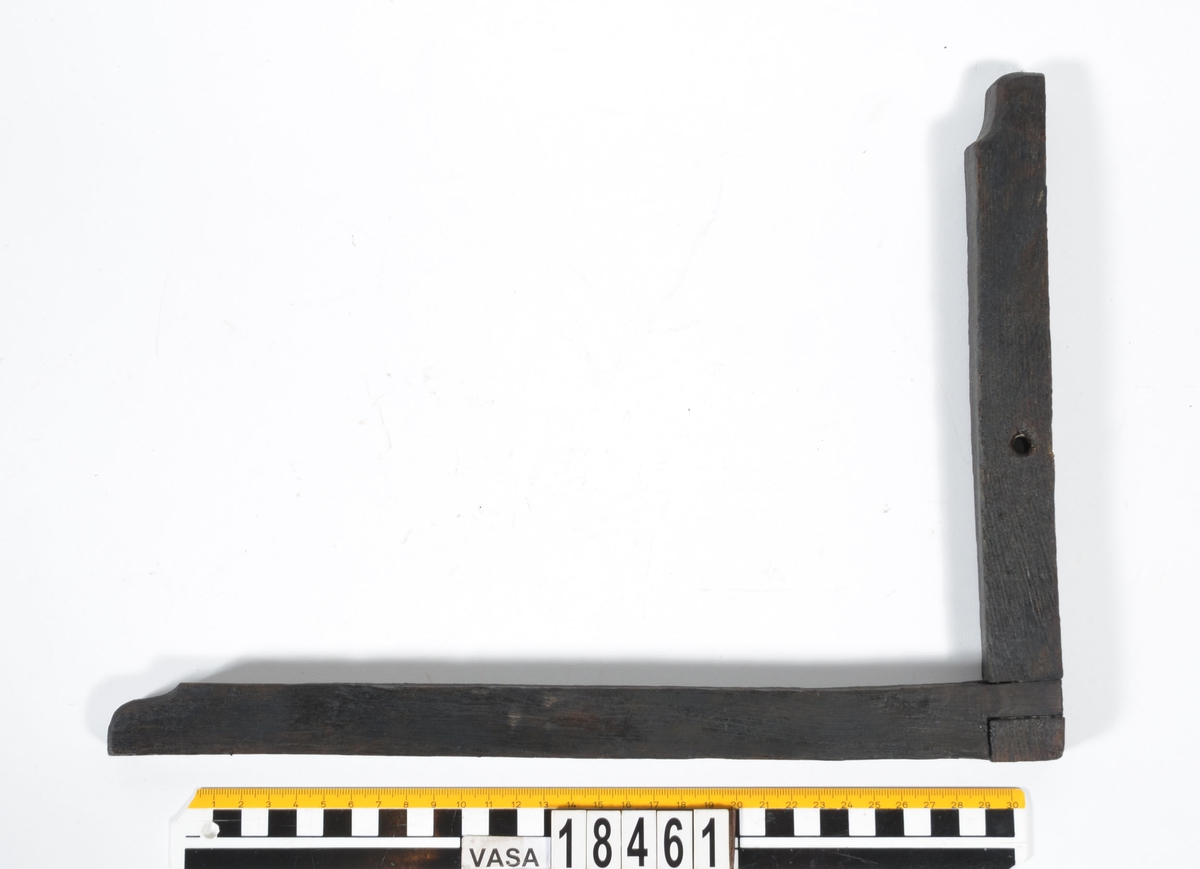 En vinkelhake.

Vinkelhaken består av två plana stavar som är sammanfogade genom sinkning. Ändarna är profilerade. I mitten av den kortare staven finns ett runt hål för upphängning.

Vinkelhaken är välbevarad och i gott skick.

För mer information se Dokumentationsblankett under Referenser – Länkade filer.