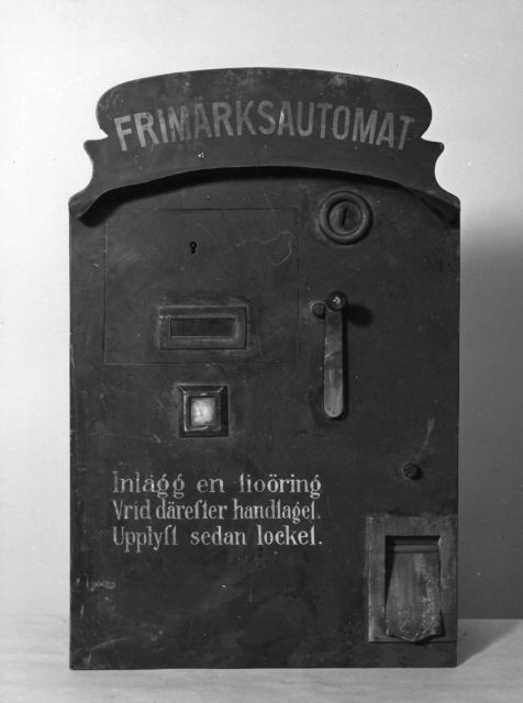 Frimärksautomat för tioöres frimärken. Mörkblå med vit text:
Inlägg en tiöring. Vrid därefter handtaget. Upplyft sedan locket.