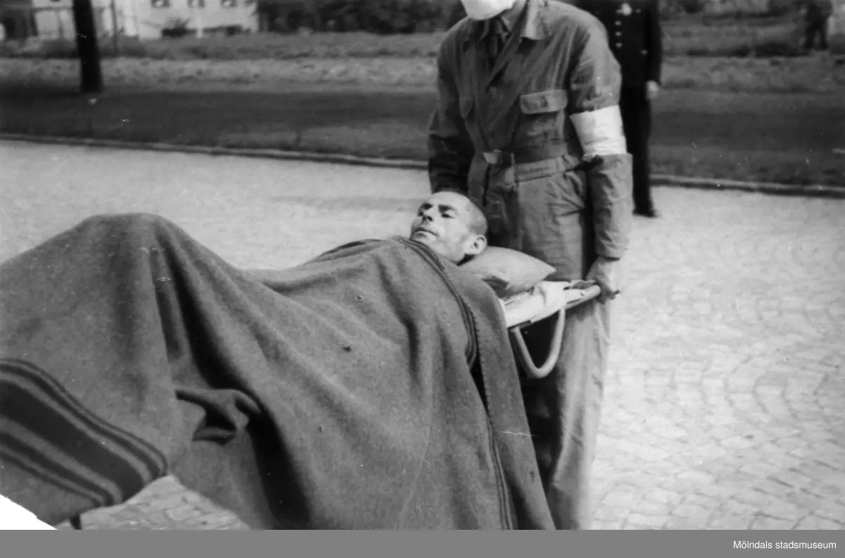"Karantänsförläggning" på Kvarnbyskolan för överlevande från koncentrationsläger i Tyskland och Polen 1945.  
Skolan fungerade under denna sommar som beredsskapssjukhus.

Manlig flykting på bår, buren av Röda Korsets personal.