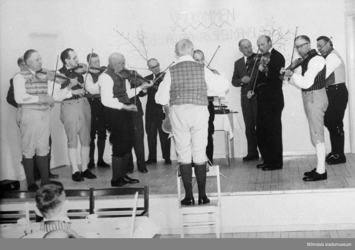 Välkommen Hällesåkers spelmanslag, står det skrivet på väggen.
Hällesåkers spelmanslag 1961.