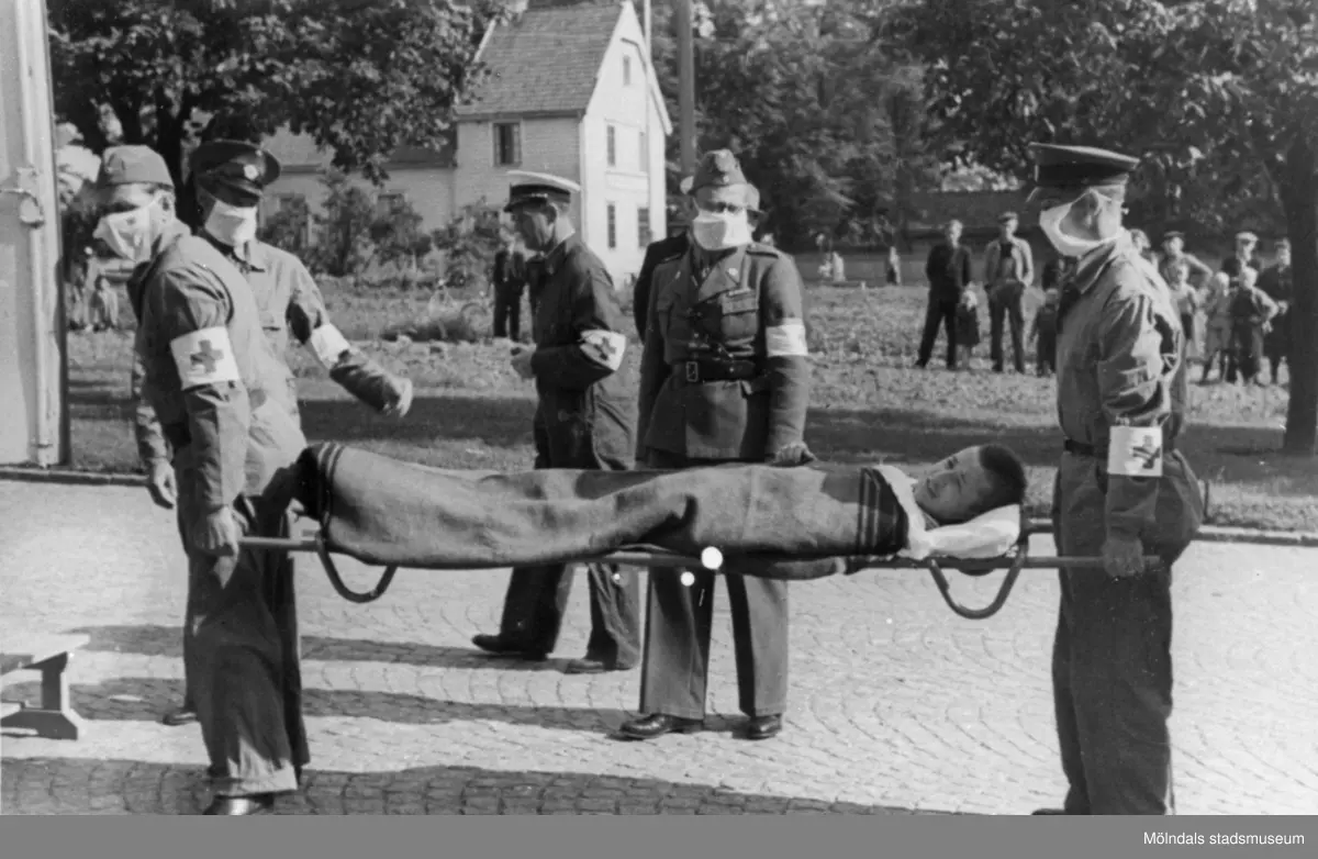 Flykting från koncentrationsläger förs till karantänsförläggningen i Kvarnbyskolan 1945. Röda korsets personal bär den sjuke på bår. I bakgrunden ses Frälsningsarméns byggnad på Kvarnbygatan 19 (idag: Kvarnbygatan 6).